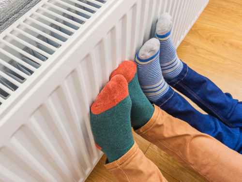 Two people warming their feet on a home radiator.
