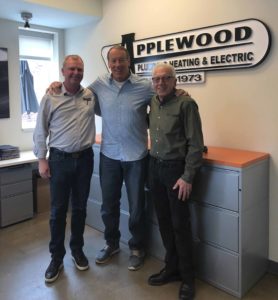 Three Applewood workers standing arm in arm in front of an Applewood sign