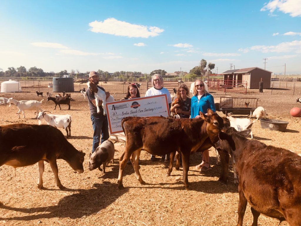 Recipients of the Caring Community giveaway standing in a pasture with various farm animals holding the check from Applewood