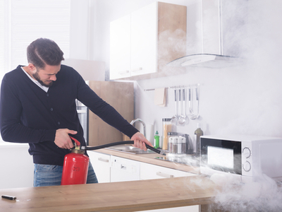 A man puts out a kitchen electrical fire with a fire extinguisher.