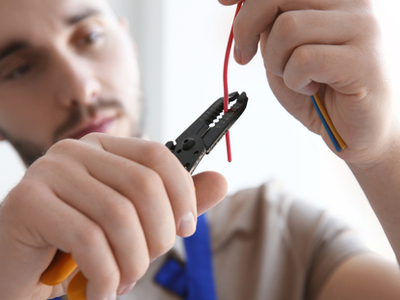 Man using wire clipper to cut a red electrical wire
