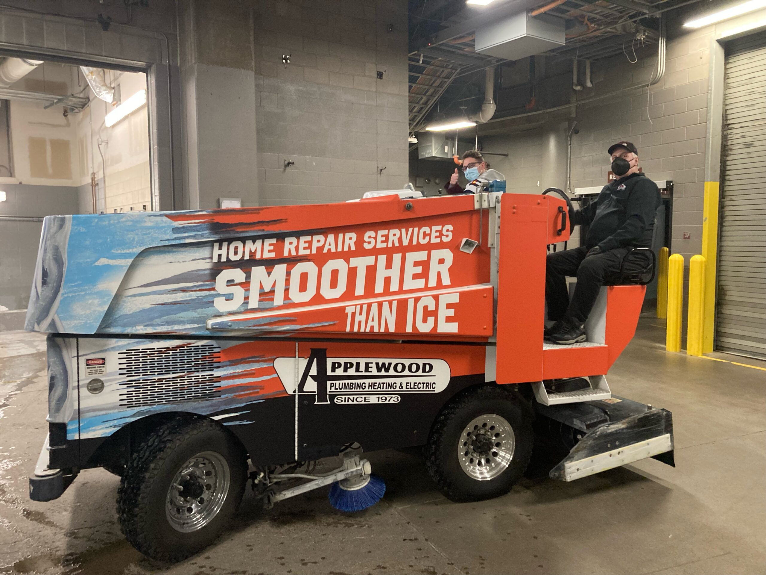 A man and a woman riding on the Applewood Zamboni