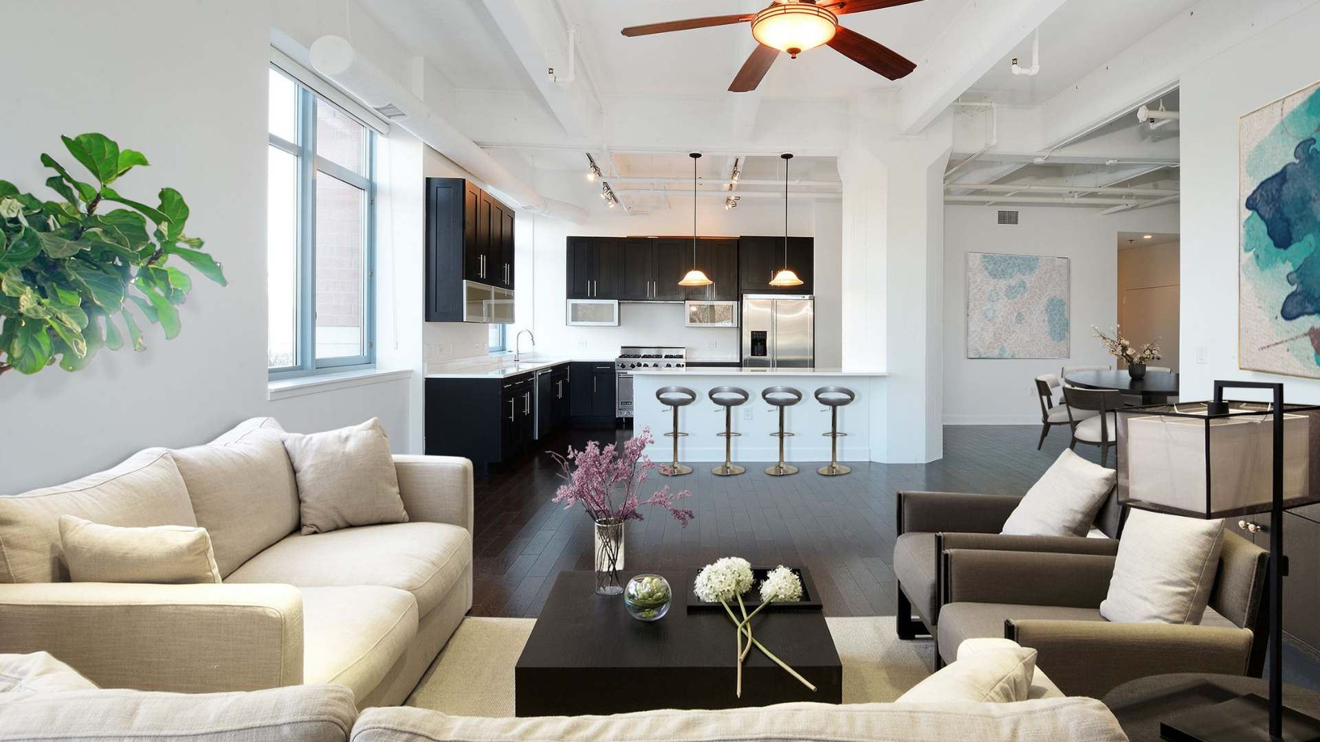 View of a modern living room and kitchen with dark wood floors and a cream couch