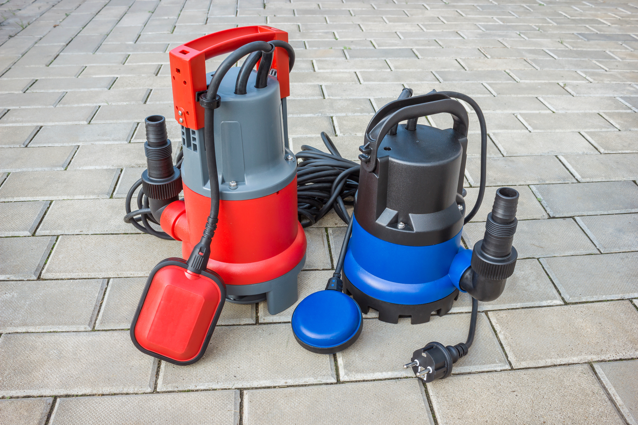 A red and blue household submersible pump sitting on a stone floor