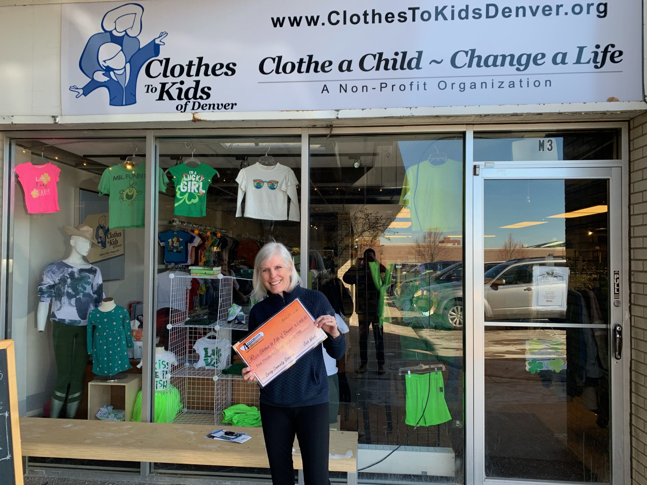 Applewood Caring Community winner standing in front of a Clothes to Kids of Denver store.
