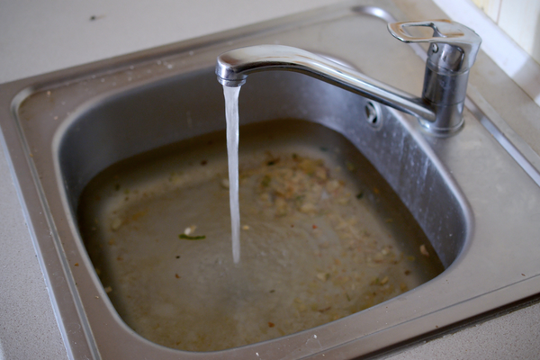 A clogged kitchen sink filled with grime and water.