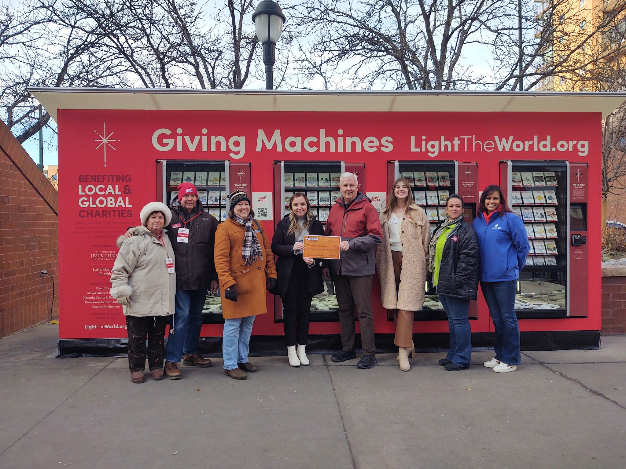 People standing and smiling in front of a giving machines stand. Two are holding an Applewood certificate.