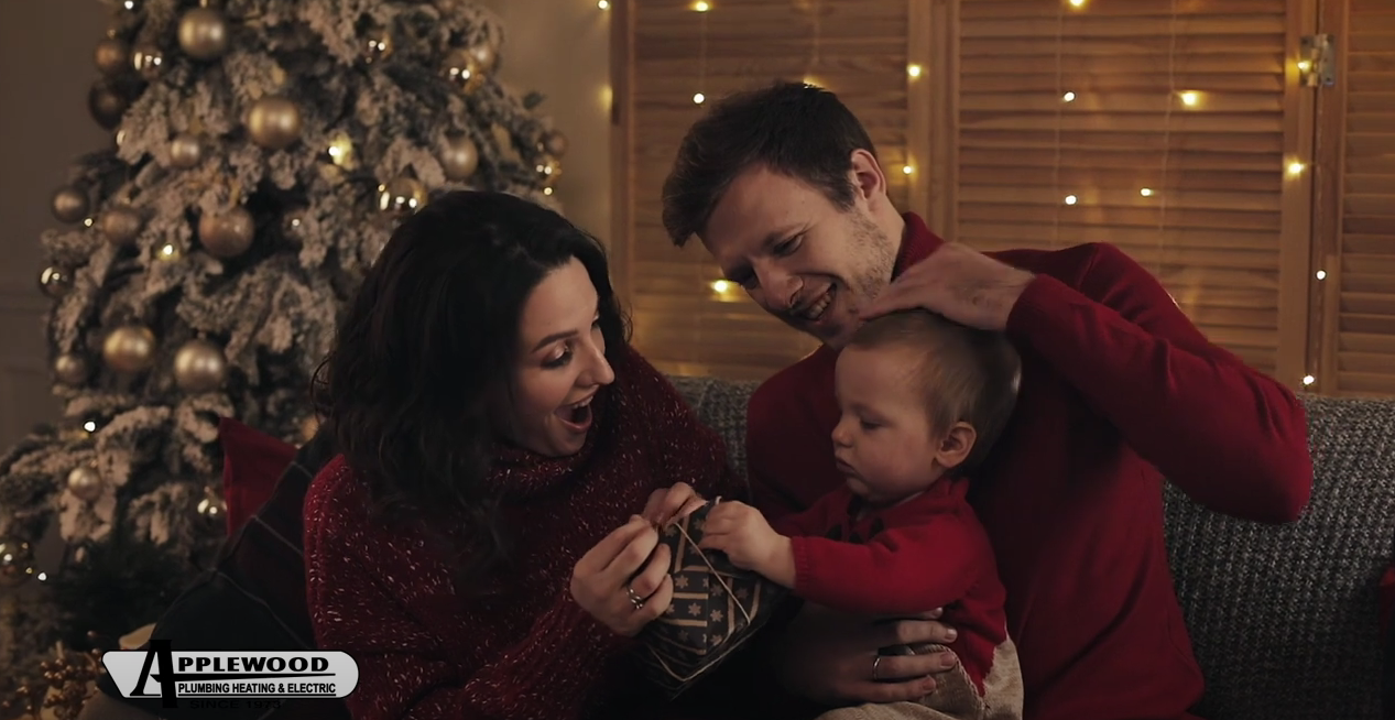 People sitting on a couch and smiling/holding a baby in front of a Christmas tree.