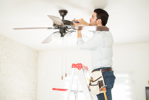 A licensed electrician installs a ceiling fan in a home.