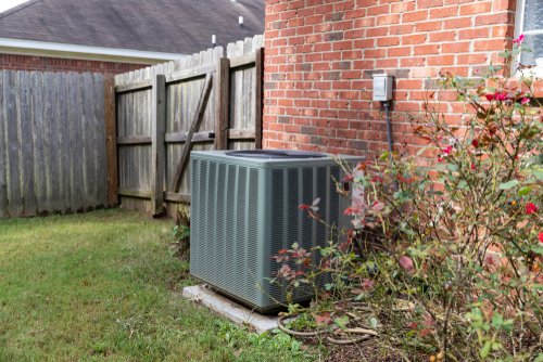 An air conditioning unit with the nicely trimmed landscaping around it.