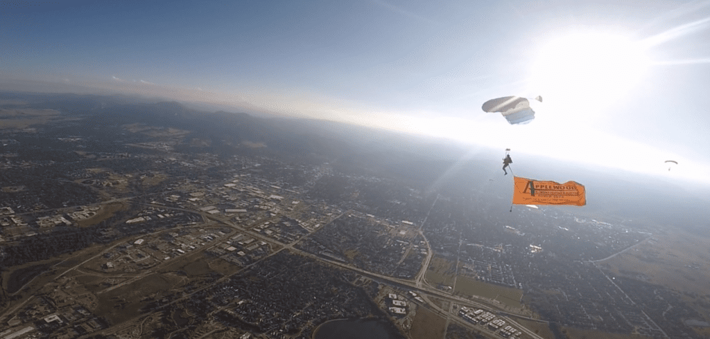 A paraglider above Denver with the Applewood banner.