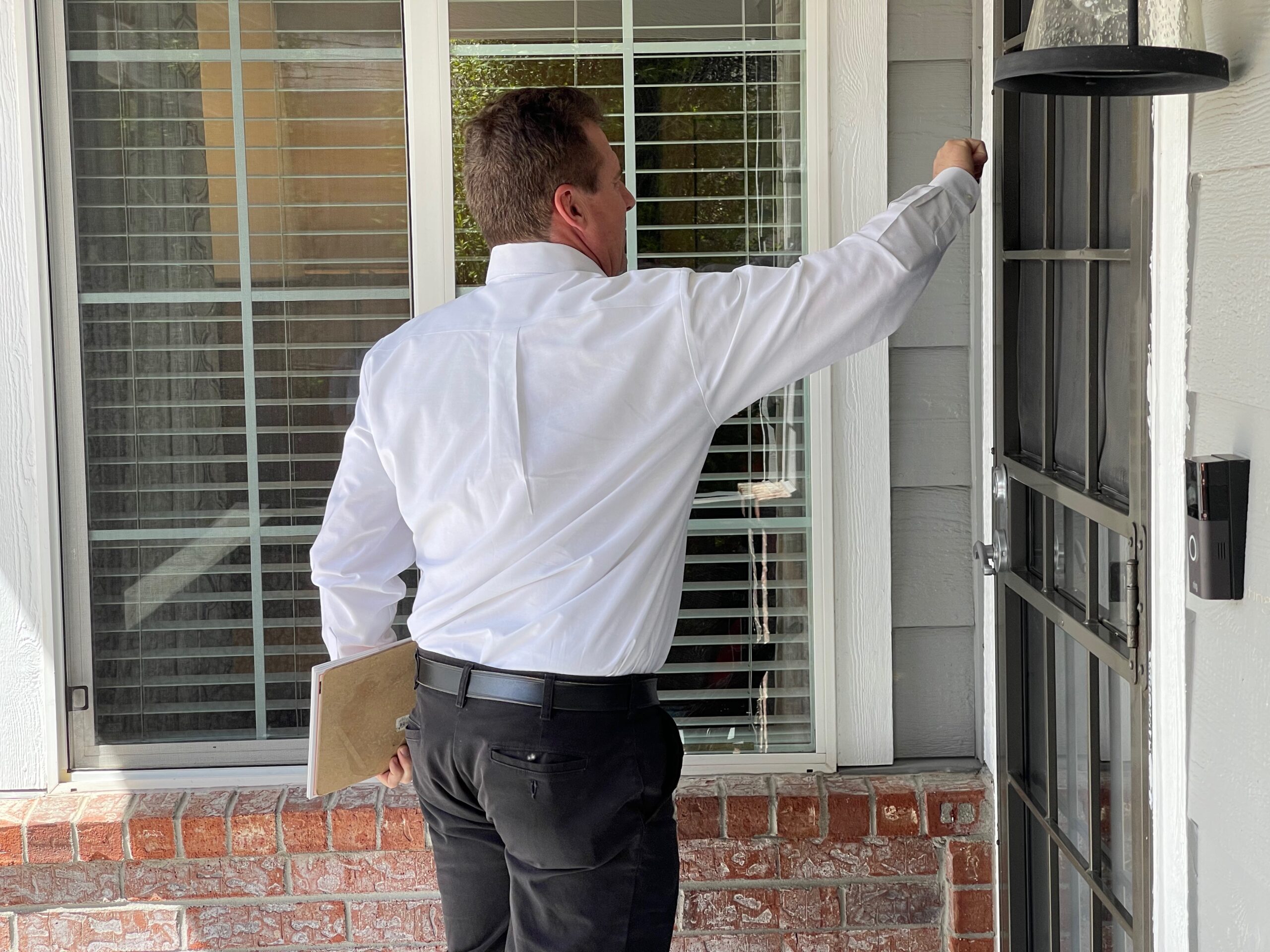man in a white shirt holding a clipboard and knocking on the front door of a house