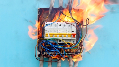 An electrical panel is on fire against a bright blue wall.
