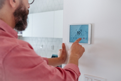 A man adjusts a smart home IoT device on the wall.