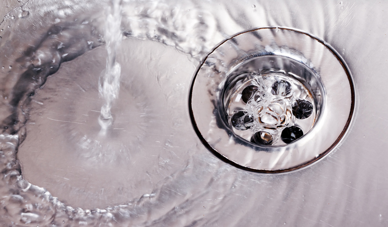 Stainless steel sink plug hole close up with water