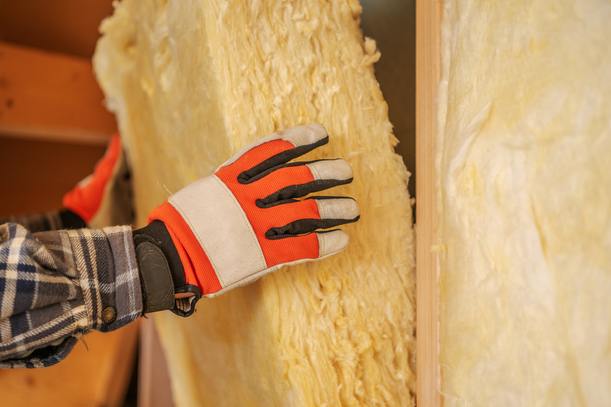 A construction worker uses gloved hands to fit insulation